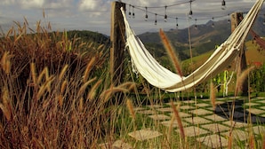 A hammock strung between wooden posts in a garden with a checkered stone pathway and grassy areas.
