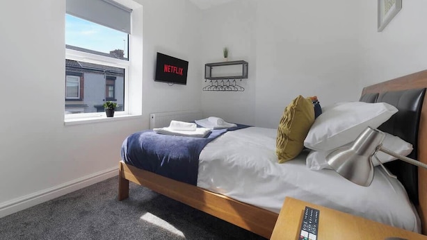 Ein Schlafzimmer mit Bett, Fernseher, Fenster, Ablagefläche und Lampe.