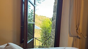 Quarto com cama, janela com vista para área verde e escada.