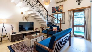 A modern living room with a staircase, a television, seating area, and a view through the door. - Goan Hideaway - Tres (Arpora)