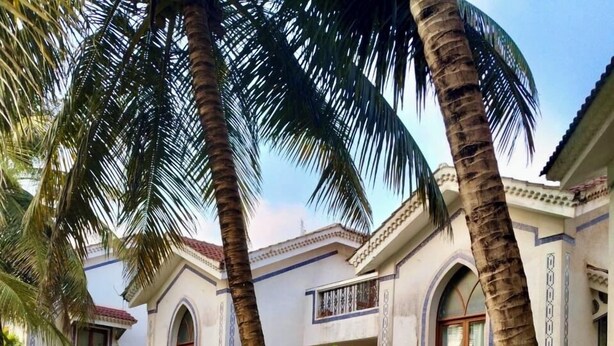 A building with arched windows and a balcony, surrounded by palm trees and a well-maintained garden. - Goan Hideaway - Tres (Arpora)