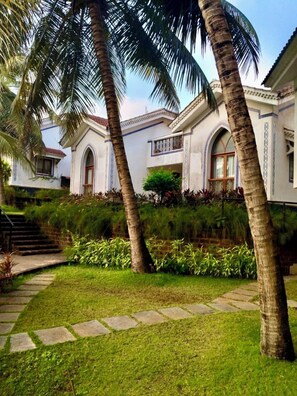 A building with arched windows and a balcony, surrounded by palm trees and a well-maintained garden.