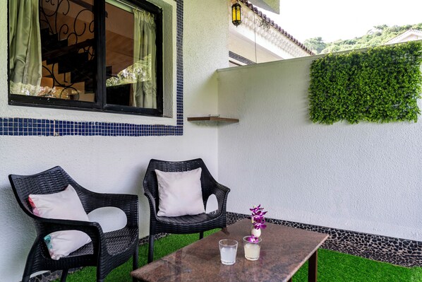 A patio with two wicker chairs, a table, and a glass of water.