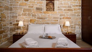 Een kamer met een stenen muur, een bed met witte lakens, twee bedlampen en een dienblad met een kopje en gebak.