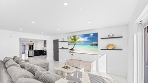 Ein modernes Wohnzimmer mit großem Flachbildfernseher, einer Couch, einem Couchtisch und einer Küche im Hintergrund.