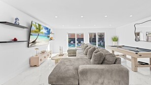 Ein modernes Wohnzimmer mit einem großen Ecksofa, einem Billardtisch und einem an der Wand befestigten Fernseher.