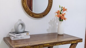 A wooden console table with a mirror, books, a vase with flowers, and a wicker basket. - Kays Place Zanzibar (ZANZIBAR)