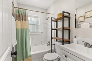 Une salle de bain avec une baignoire, des toilettes et un meuble-lavabo avec des étagères.