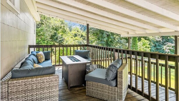 A covered outdoor seating area with wicker furniture and a table, overlooking a lush green landscape.