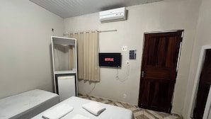 Une chambre d’hôtel avec un lit, un petit réfrigérateur, un téléviseur affichant le logo « NETFLIX », une porte et un sol carrelé.