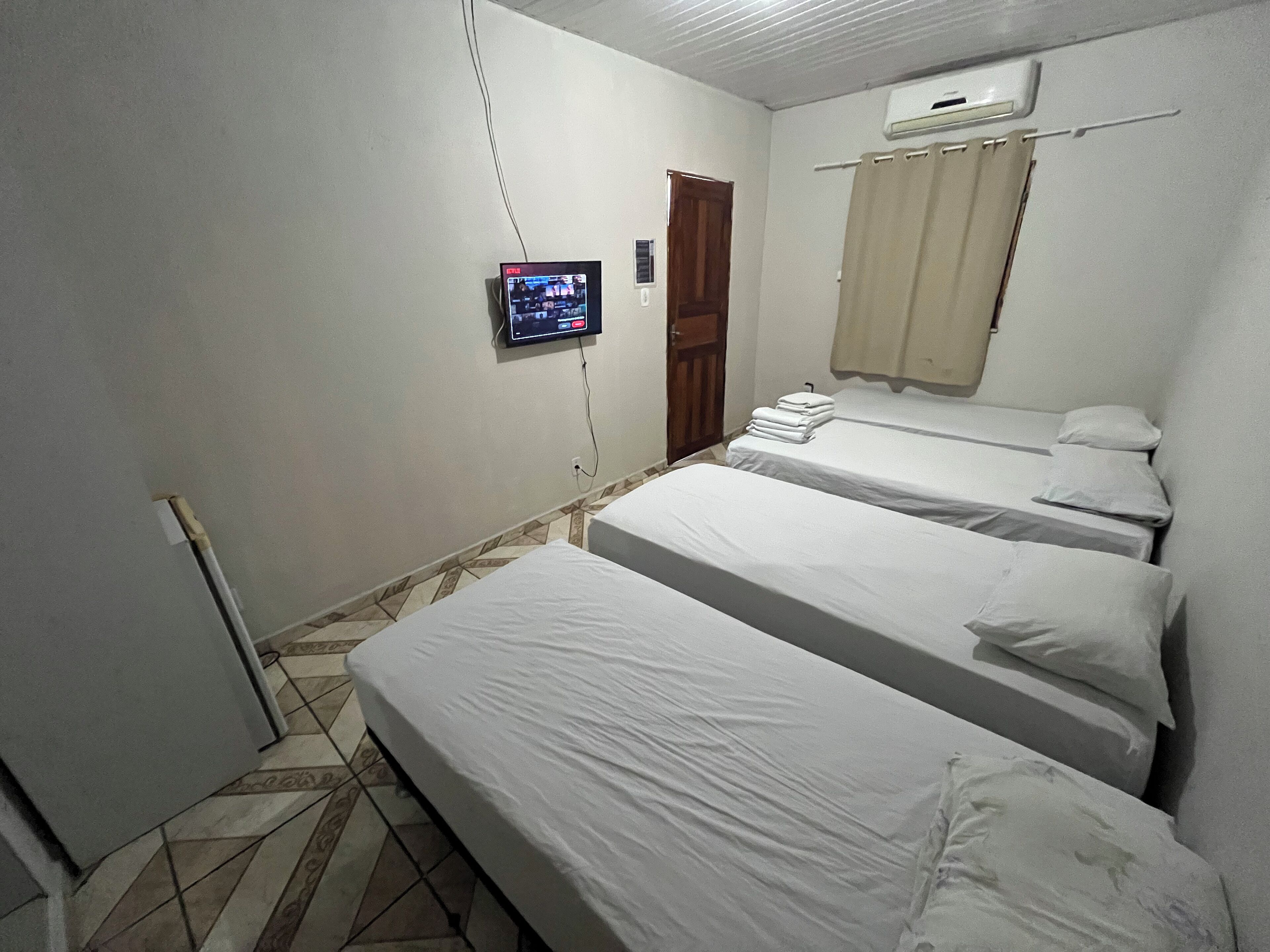 A hotel room with three beds, a TV mounted on the wall, and an air conditioning unit.