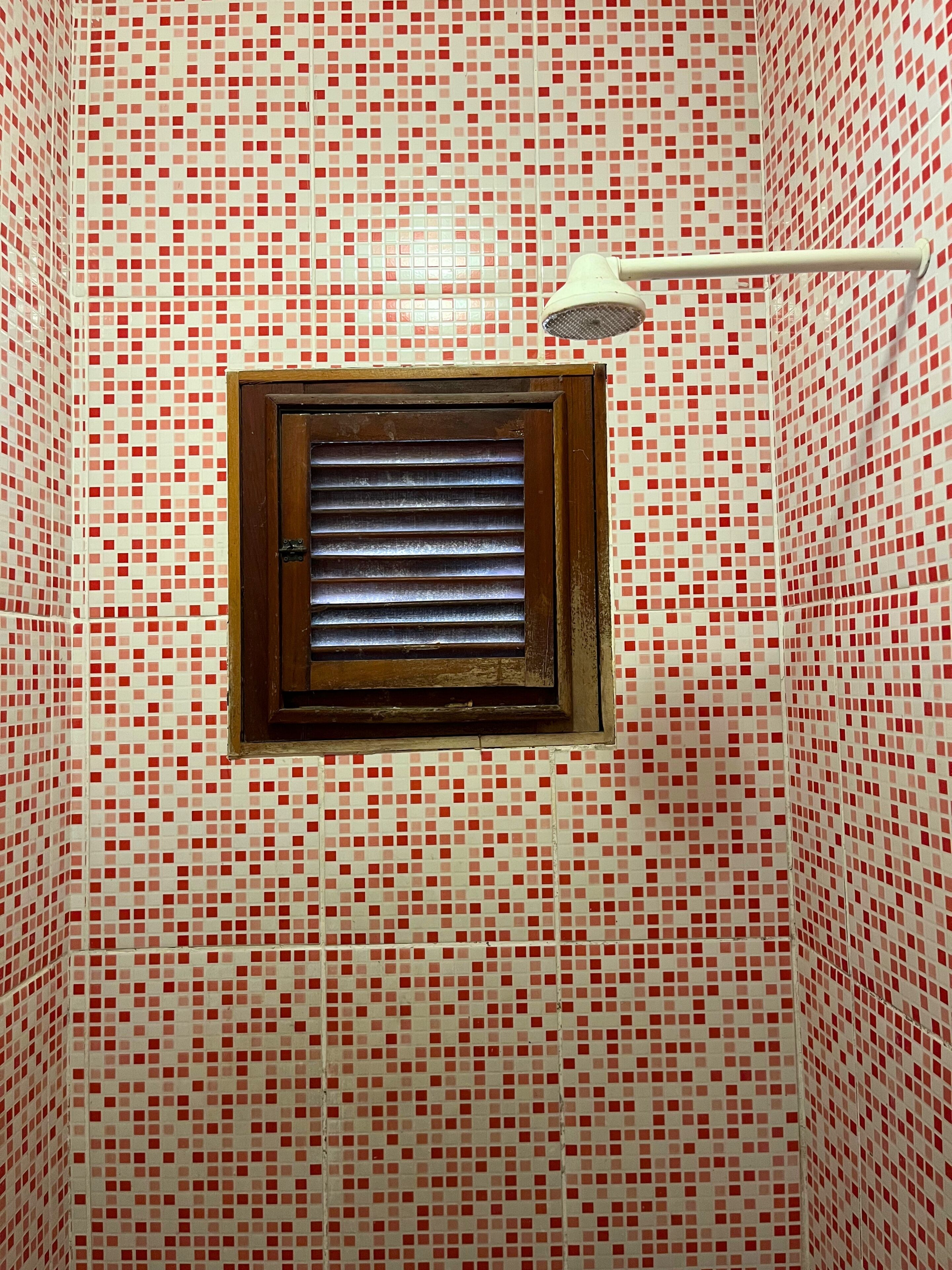 Une salle de bain avec un mur recouvert de carreaux aux motifs rouges et blancs, une fenêtre avec des stores et un porte-serviettes blanc.