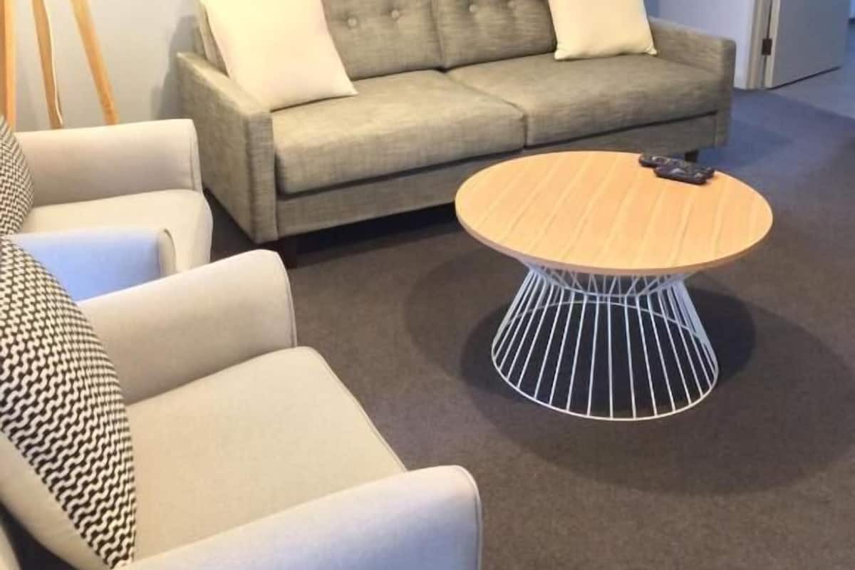 Una sala de estar moderna con un sofá gris, dos sillones blancos, una mesa de centro redonda y dos cuadros colgados en la pared.