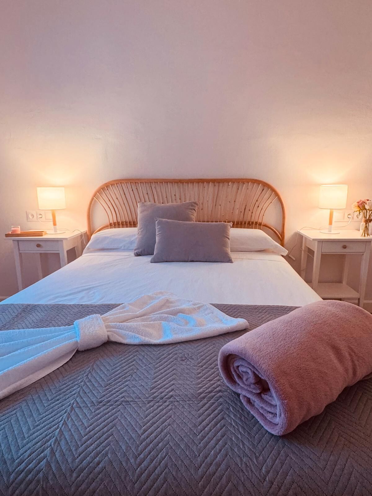 Cama bem arrumada com cabeceira de madeira, duas almofadas e uma toalha dobrada.