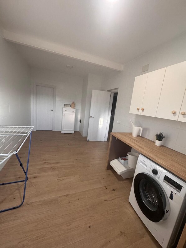 A laundry area with a washing machine, a drying rack, and a wooden counter with a sink.