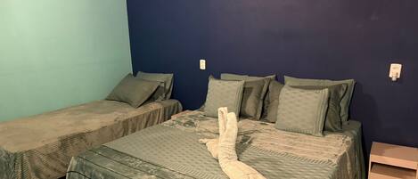 A room with two beds, each with a green bedspread and matching pillows. There is a small bedside table with a drawer on the right side.