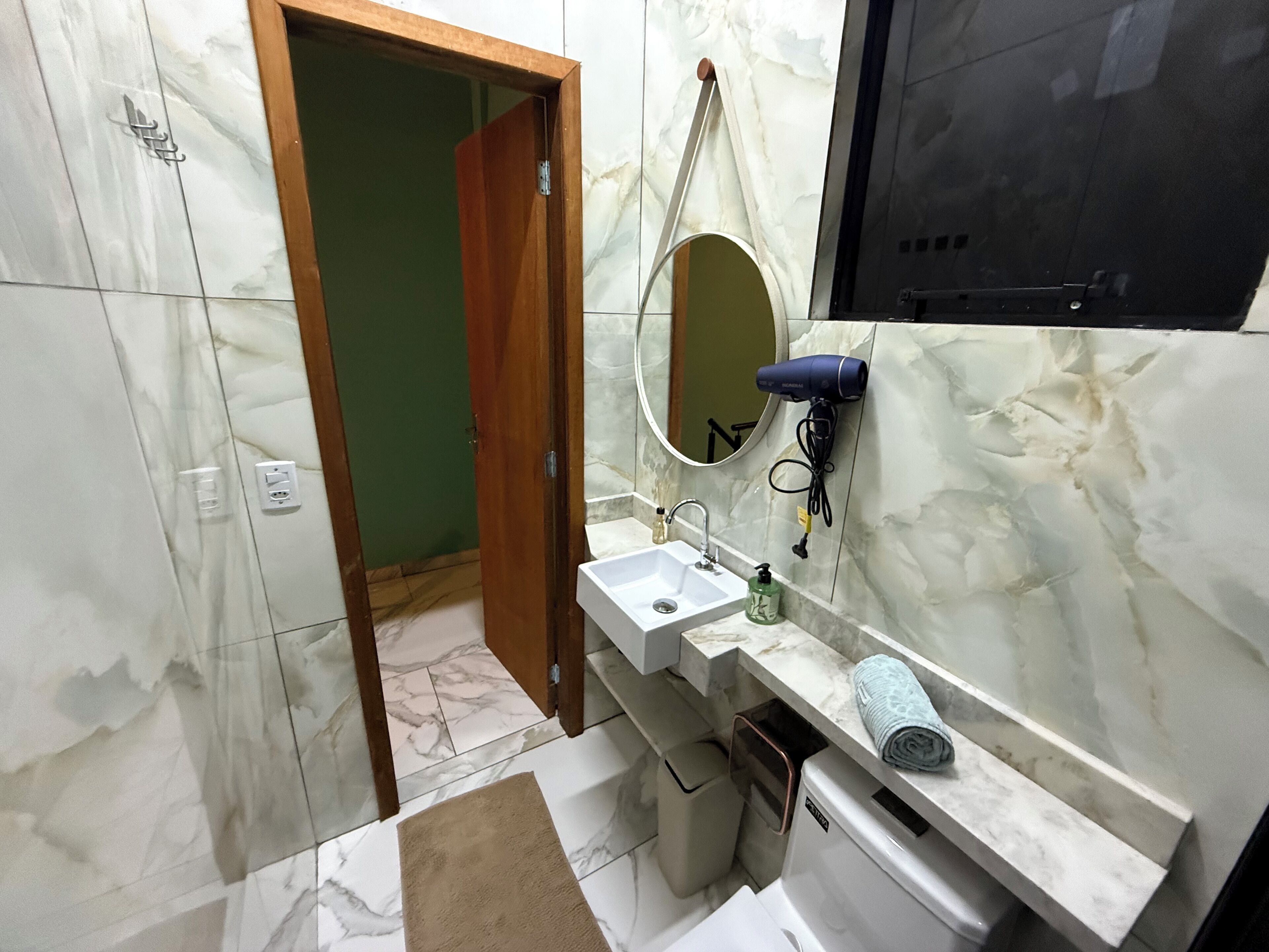 A bathroom with a marble floor, a wooden door, a sink with a mirror, a hairdryer, and a towel.