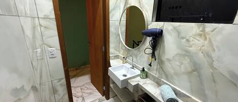 A bathroom with a marble floor, a wooden door, a sink with a mirror, a hairdryer, and a towel.