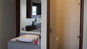 A bathroom with a white toilet, a sink with a mirror above it, and an air conditioning unit on the wall. - Hotel & Villas HANGAR  (Colon)