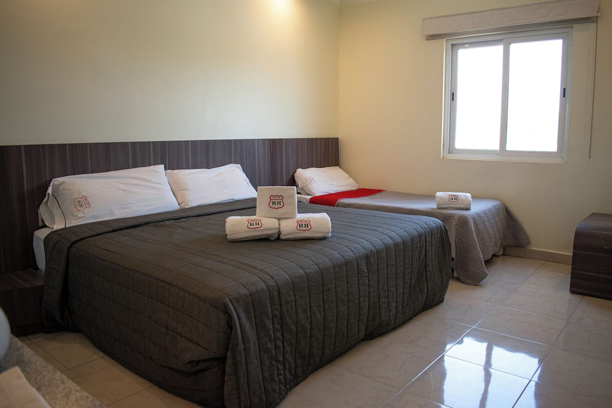 A hotel room with two beds, a window, and a bedside table.