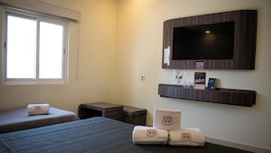 A hotel room with two beds, a TV mounted on the wall, a small table, and a bench. - Hotel & Villas HANGAR  (Colon)