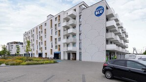 Un hotel moderno de varios pisos con un diseño circular distintivo en la fachada, un área de estacionamiento y un coche negro estacionado al frente.