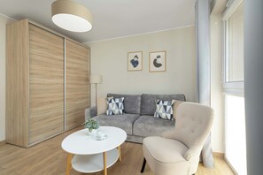Un salon moderne avec un canapé gris, une table basse blanche, un fauteuil beige, une armoire en bois et deux œuvres d’art abstraites accrochées au mur.