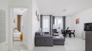 Una sala moderna con un sofá gris, un comedor con una mesa y sillas, y un televisor a la derecha.