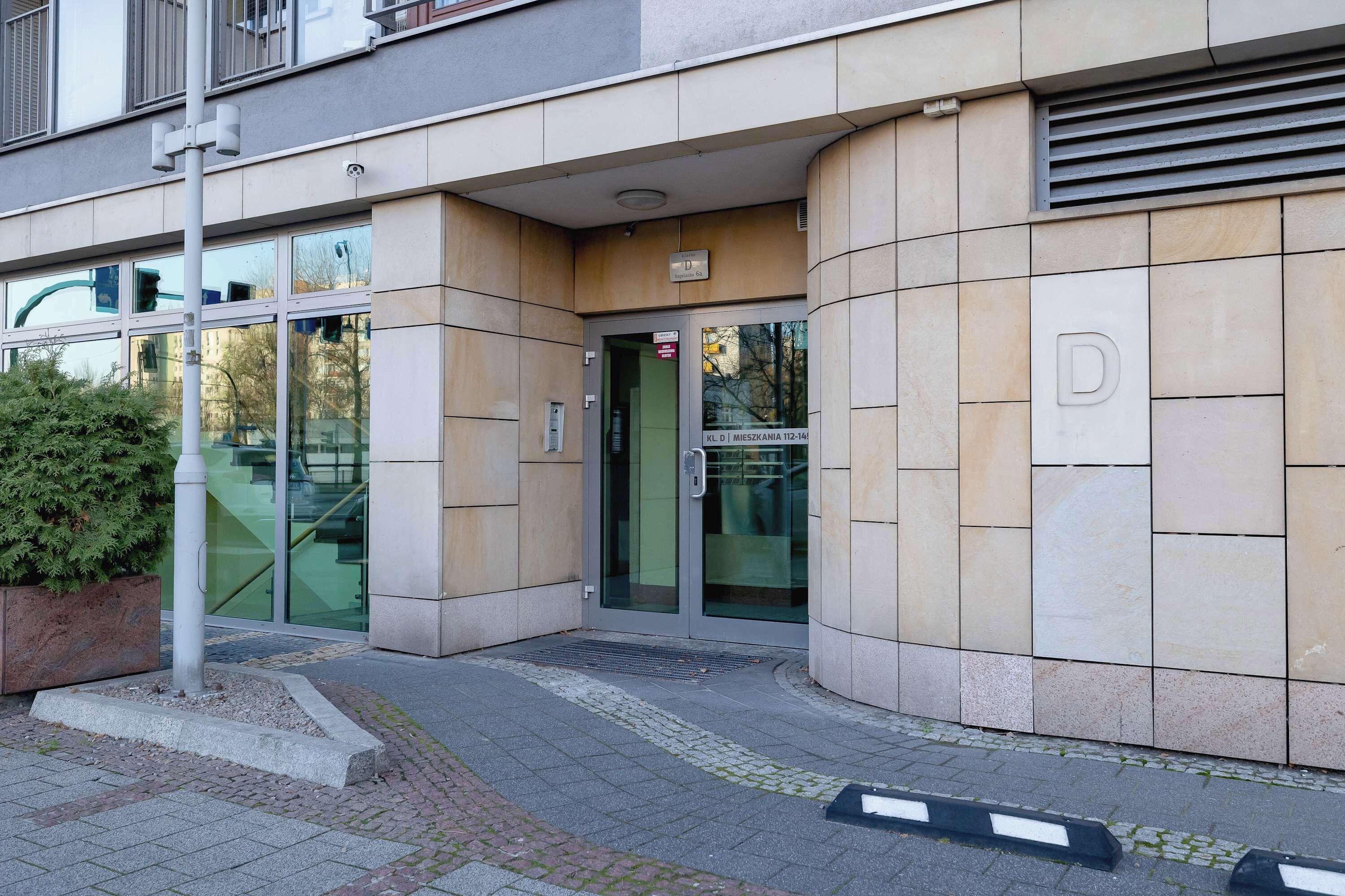 A building entrance with a glass door, a metal sign, and a tiled wall.