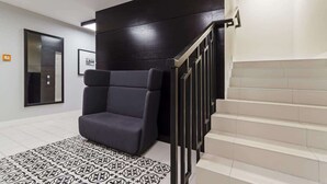 A modern interior with a dark-colored chair, a staircase with a black railing, and a patterned floor.