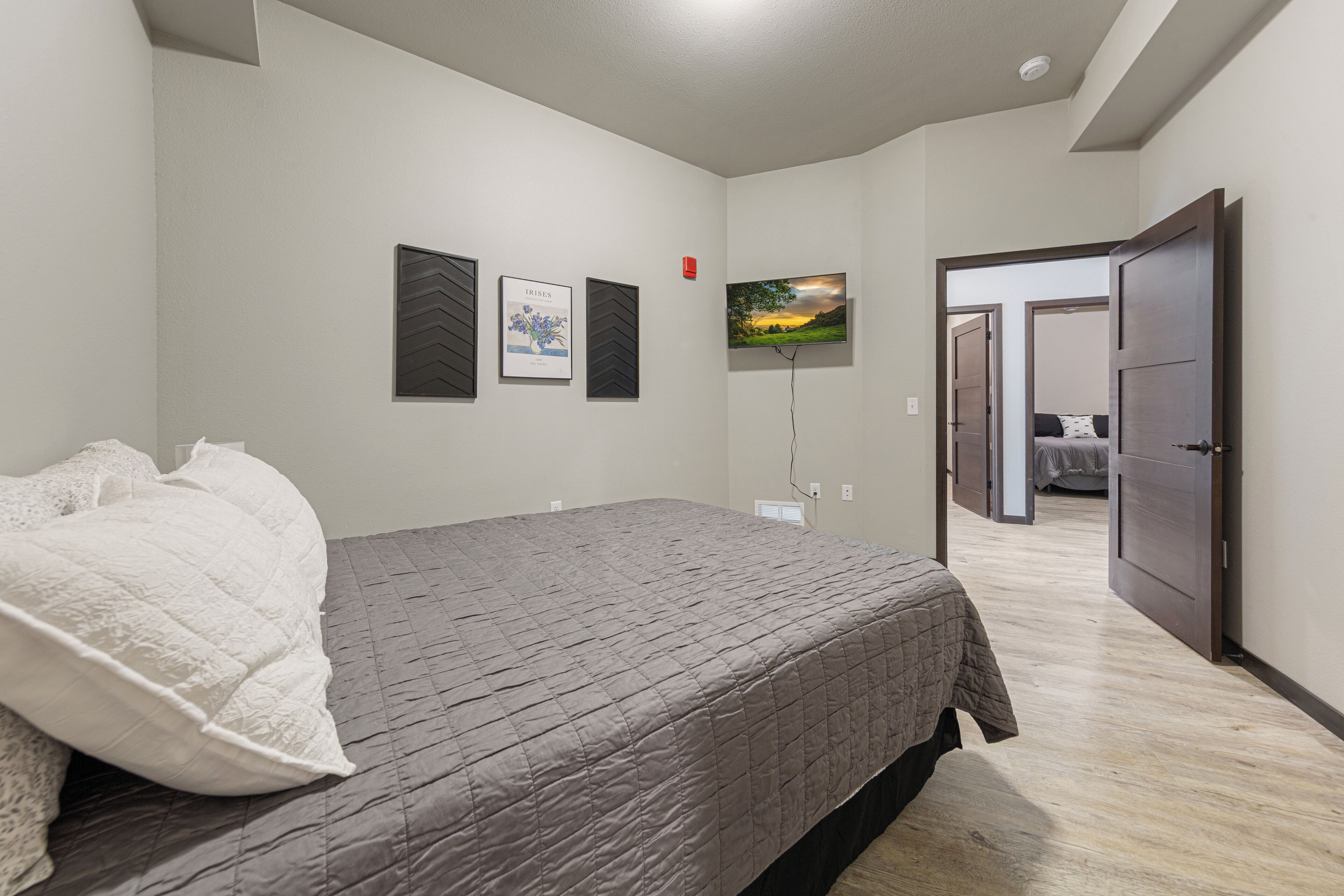 Une chambre à coucher avec un lit, un téléviseur fixé au mur et une porte donnant sur une autre pièce.