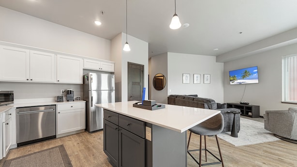 A modern kitchen with white cabinets, a stainless steel refrigerator, and a central island with bar stools. - Charming 2-bedroom/2 bath apartment with spa & fitness room amenities in Mankato (Mankato)