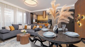 Un salón moderno con una mesa de comedor de madera oscura para cuatro personas, un sofá gris con cojines amarillos y una cocina al fondo.
