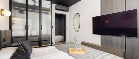 A modern hotel room with a large bed, a flat-screen TV mounted on the wall, and a sliding glass door leading to a balcony.