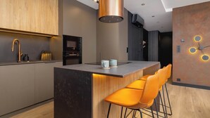 Una cocina moderna con una isla central, taburetes de bar y una lámpara colgante de cobre.