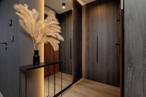 Un pasillo moderno con piso de madera, una consola negra y un florero con plumas de pampa, y puertas de madera oscura.