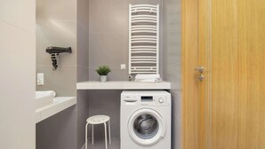 A compact laundry area with a washing machine, a drying rack, and a small stool. - Spacious Apartment | 3 Bedrooms | Parking and Balcony (Kraków)
