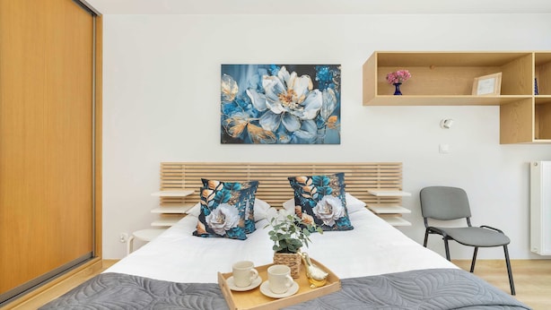 A neatly arranged bedroom with a bed, pillows, a bedside table, a chair, and a painting on the wall. - Spacious Apartment | 3 Bedrooms | Parking and Balcony (Kraków)