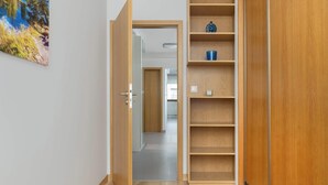 A hallway with a wooden door leading to a room, a wooden wardrobe, and a shelf with a blue object. - Spacious Apartment | 3 Bedrooms | Parking and Balcony (Kraków)
