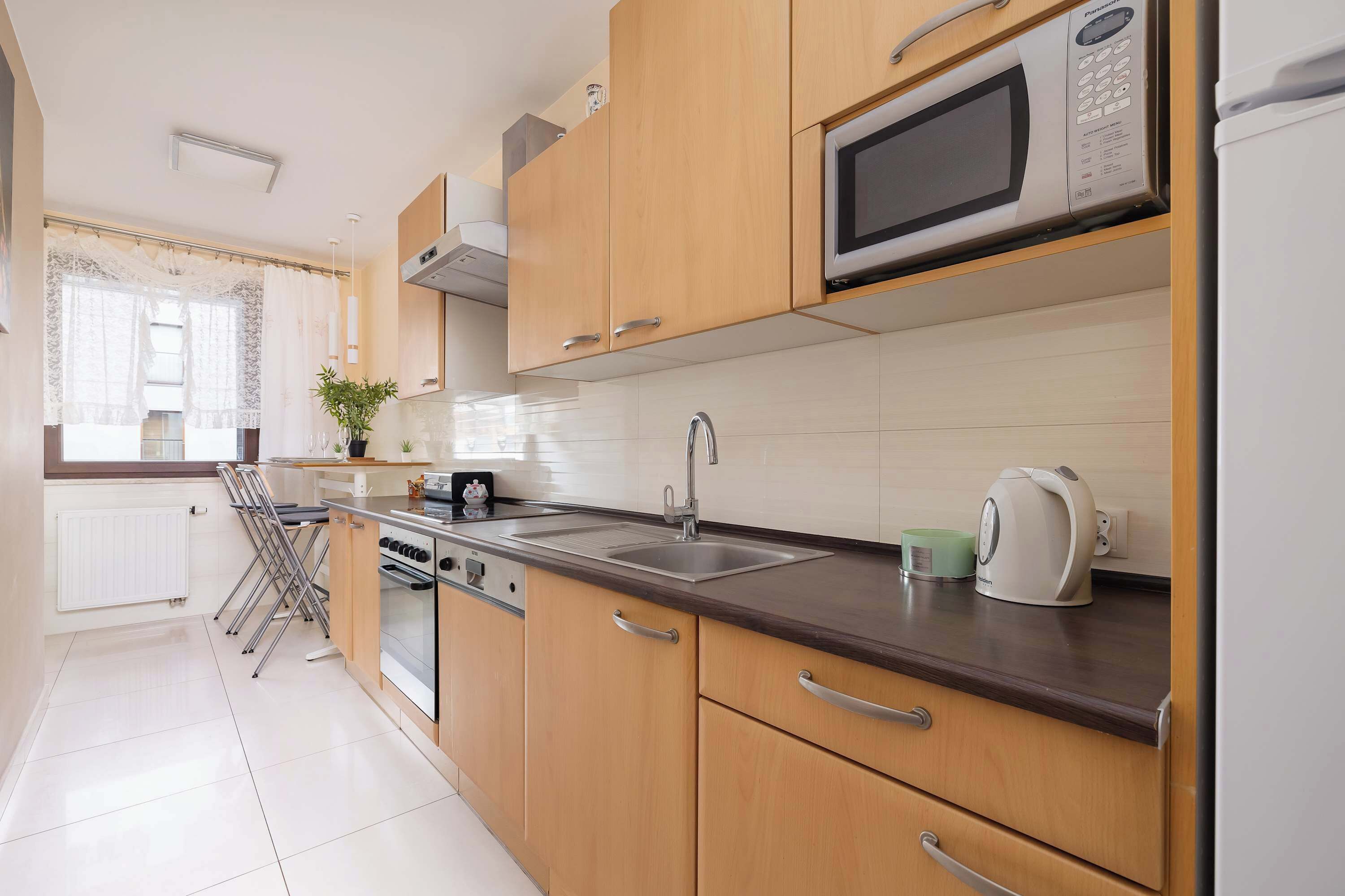 A modern kitchen with wooden cabinets, a stainless steel sink, a microwave, and a kettle.