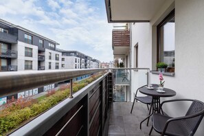 Un balcon donnant sur un paysage urbain, une table avec des chaises et une plante en pot.