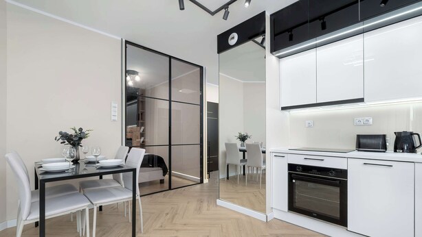 A modern kitchen with white cabinets, a built-in oven, and a dining area with a glass partition.