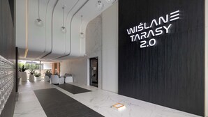 A modern lobby with a marble floor, a reception desk, and a wall with the text "WISLAN TARASY 2.0".