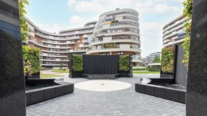 A modern apartment complex with curved balconies, a central circular plaza, and surrounding greenery.