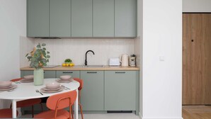 A modern kitchen with teal cabinets, a white countertop, and a dining area with a white table and orange chairs. - Cozy Studio in Praga | Balcony and Close to Metro (Warszawa)