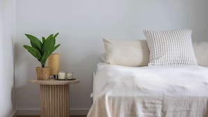 A bedroom with a bed, pillows, a bedside table with a plant and candles, and a wall. - Cozy Studio in Praga | Balcony and Close to Metro (Warszawa)