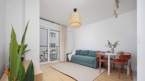 A modern living room with a sofa, dining table, chairs, and a large plant. - Cozy Studio in Praga | Balcony and Close to Metro (Warszawa)
