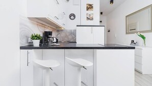 A modern kitchen with white cabinets, a black countertop, and two white bar stools. - Bright Studio in the Center | Close to Kleparski Park (Kraków)