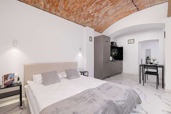 Un dormitorio moderno con techo de ladrillo, una cama grande con cabecera blanca, un sofá gris, un escritorio con silla y un armario.