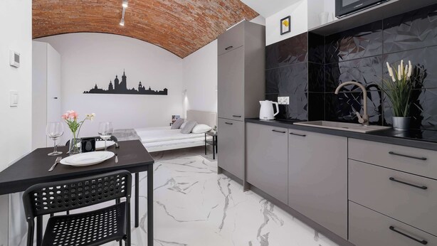 Eine kleine Küche mit Mikrowelle, Spüle und moderner Schränke. Im Hintergrund ist ein Bett mit Stadtbild-Wandgemälde zu sehen.